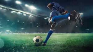 Football or soccer player in action on stadium with flashlights, kicking ball for winning goal, wide angle. Action competition in motion