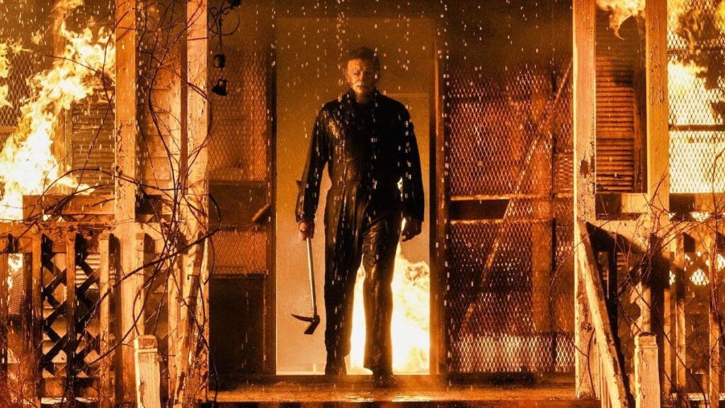 killer michael myers standing on porch of burning house