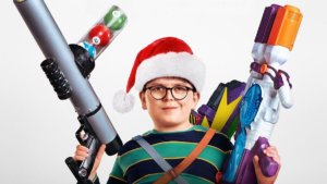 A mischievous child in glasses wearing a santa hat and holding toy guns
