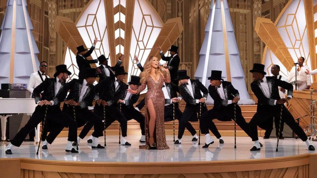 Mariah Carey on stage in a sparkling dress with a group of male dancers behind her