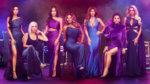 Seven elegantly dressed women in purple and blue gowns