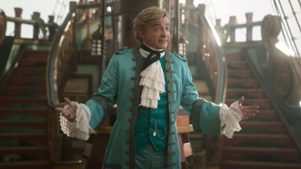 A man in 18th century garb shrugs on a ship