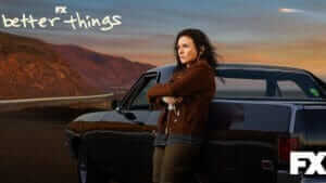 A woman leans against a vintage car in a western mountain landscape