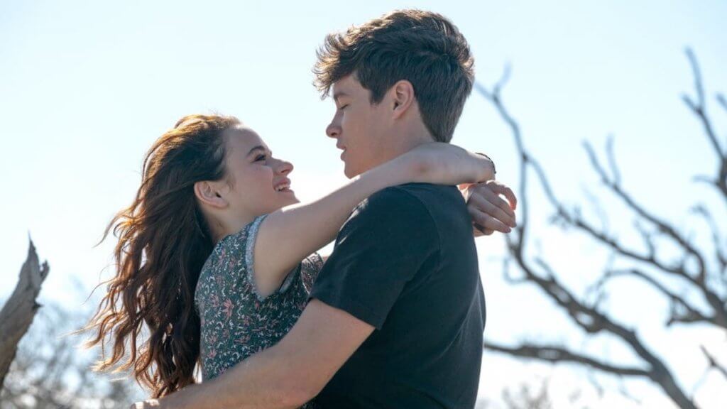 A young teen couple embrace on the beach by a driftwood tree