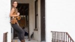 A woman in work clothes leans on the doorway of a house mid-renovation