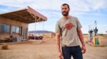 A man stands in front of a desolate gas station in the Australian outback