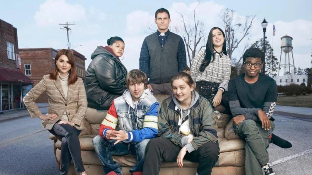 The cast of Flatch sits on a couch in the street