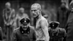 An emaciated man in a boxing circle surrounded by Nazis