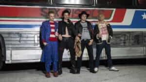 Four men dressed in punk clothes lean against a bus