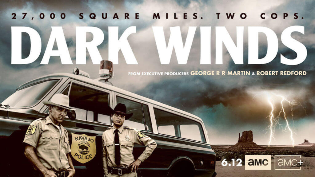 Two police officers stand in front of an old car in a thunderous dessert landscape