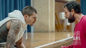 A tattooed basketball player leans in to talk with a scruffy Adam Sandler