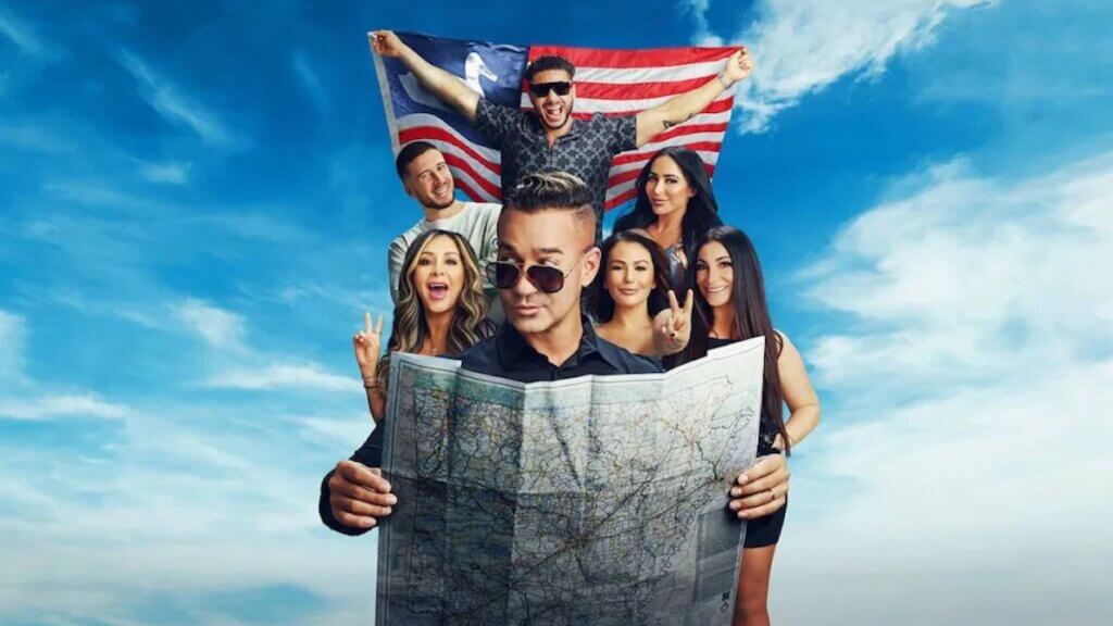 A group of reality stars gathered behind a road map and in front of a US flag and blue sky