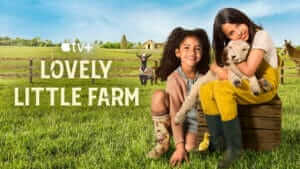 two young girls sit on a farm yard, snuggling a lamb