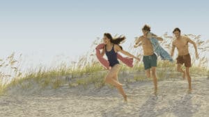 Three teens run down a beach