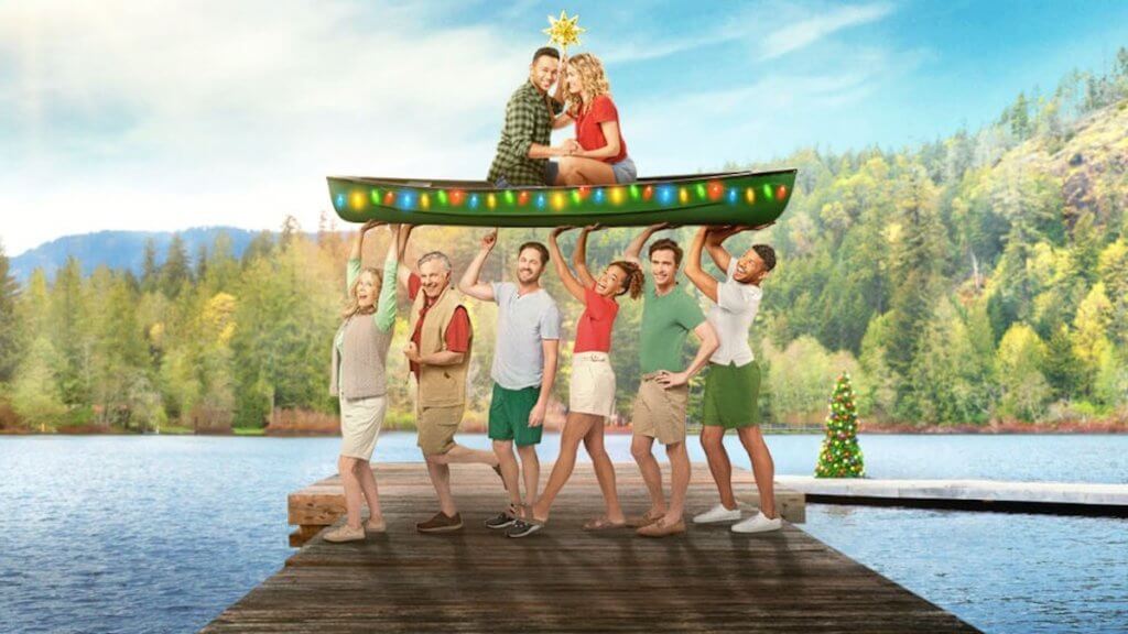 A group of friends holds a canoe trimmed like a Christmas tree on a dock, with a couple to top holding the star