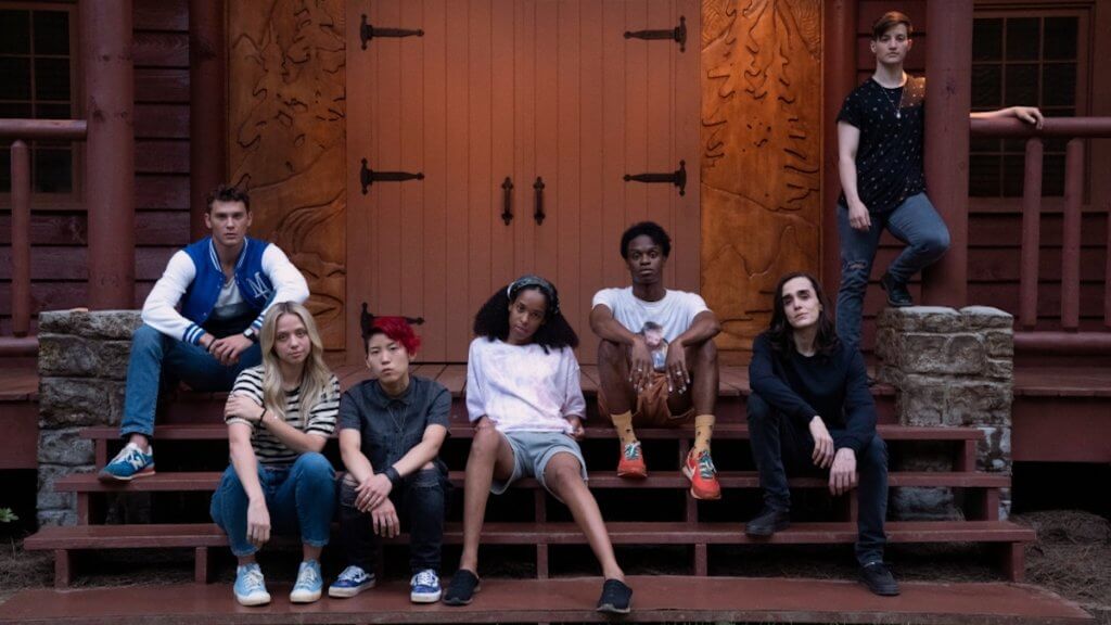 A group of queer teens on the steps of a lodge building