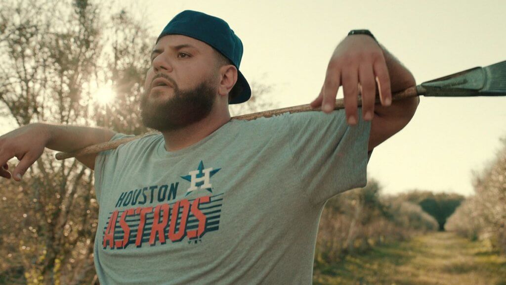 An Arab-American man holding a rake wearing a Texas Astros shirt