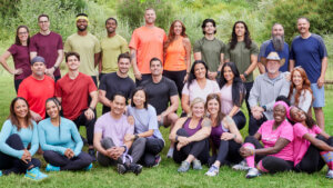 13 pairs of competitors in solid colored tee shirts pose in a group