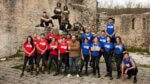 Two teams in red and blue shirts stand in old stone ruins