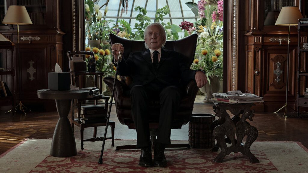 Donald Sutherland sits in a chair looking ominous in a black suit