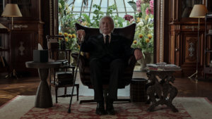 Donald Sutherland sits in a chair looking ominous in a black suit
