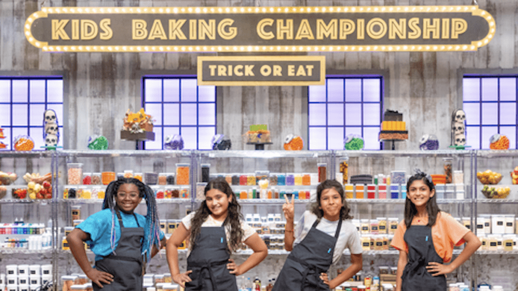 Four kid bakers in front of a row of halloween colored candies