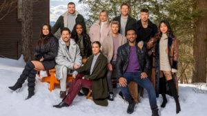 A group of good looking people sitting and standing in a group in a snowy landscape