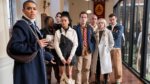 A group of posh prep school kids in a hallway turned in surprise looking past the camera