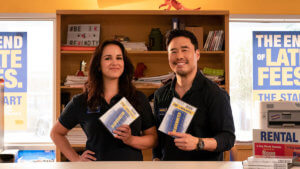 A woman and man stand in a video stop holding up DVDs