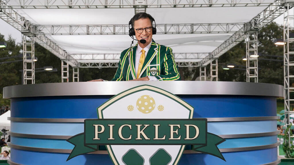 Stephen Colbert behind a sports desk with an announcer's headset on