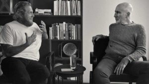 Two men sit facing each other and chatting in a black and white shot