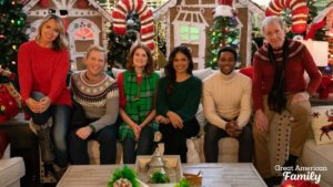 Five people in winter sweaters sit in front of a large Christmas display