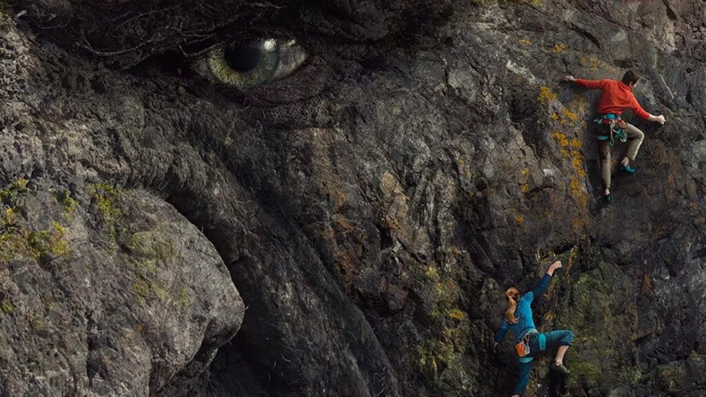 Two climbers scaling a rock face with a literal eye and face