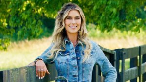 A blonde woman in denim stands by a farm fence