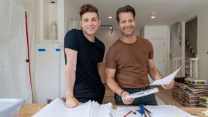 Two handsome men leaning on a table full of home plans in the center of a home renovation.