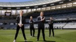 Four athletic judges stand on a large stadium field