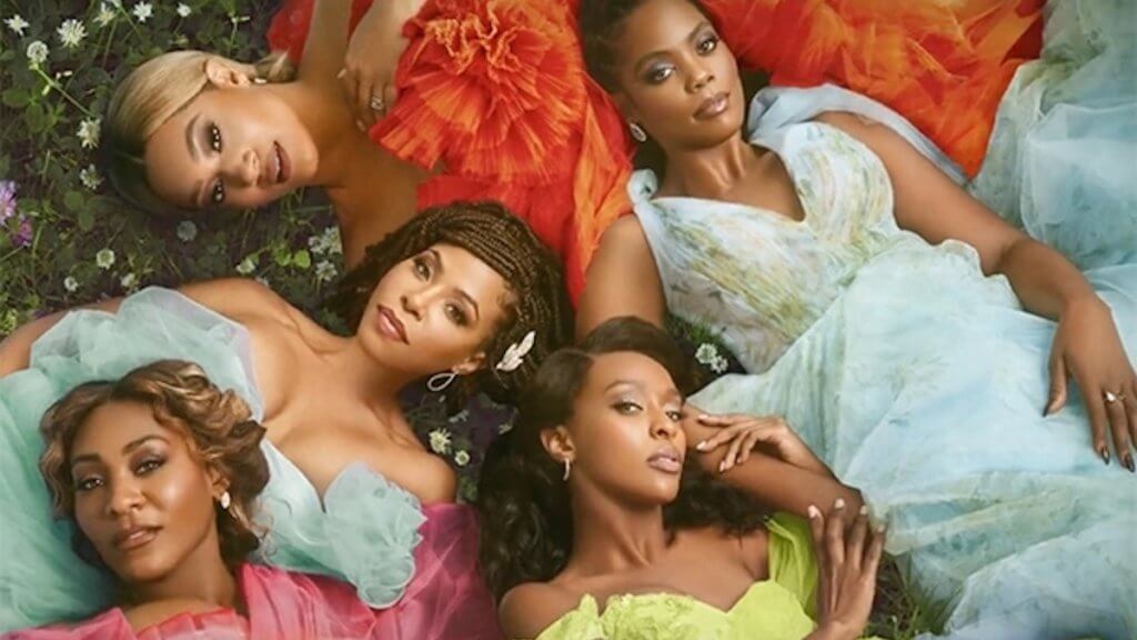 Five black women laying in a pile of fluffy pastel dresses in a garden