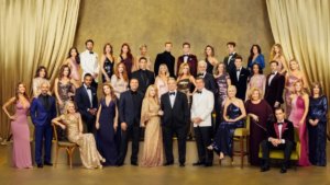 A large group of soap opera stars in formal wear in front of a gold draped set.