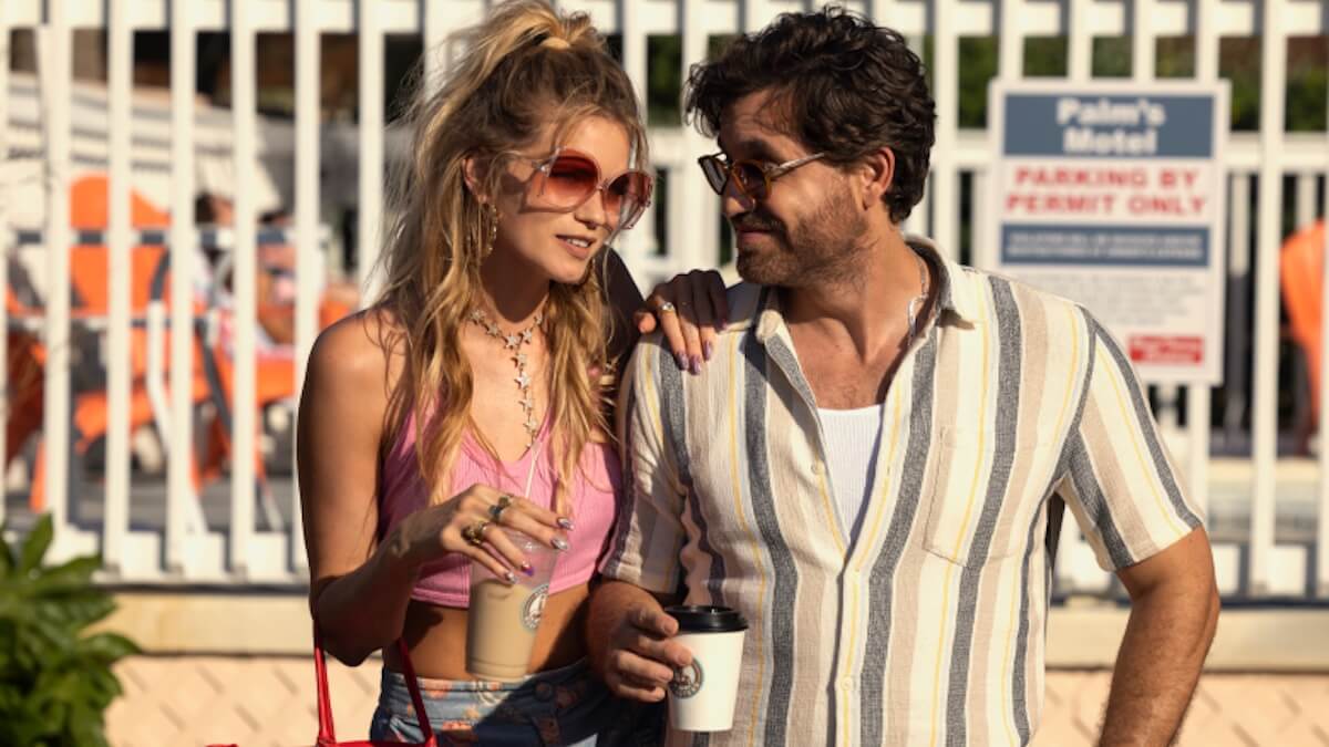 A couple in summery clothes and sunglasses walk on a beach