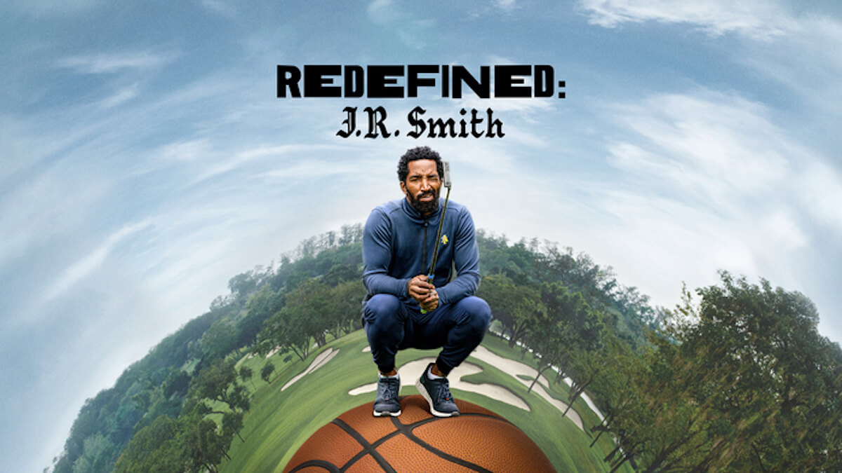 A man perches on top of a basketball in golf gear in front of a domed golf course.