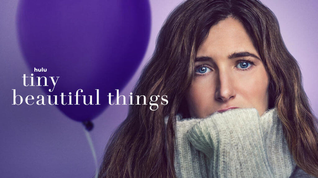 A woman huddled in an oversized turtleneck seater in front of a purple balloon