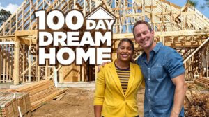 A couple stands in front of a framed out home under construction
