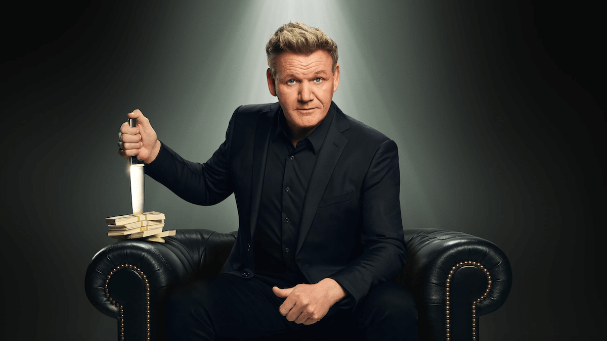 Chef Ramsay in a black suit and sitting in a black leather chair holding a chef's knife through a stack of cash