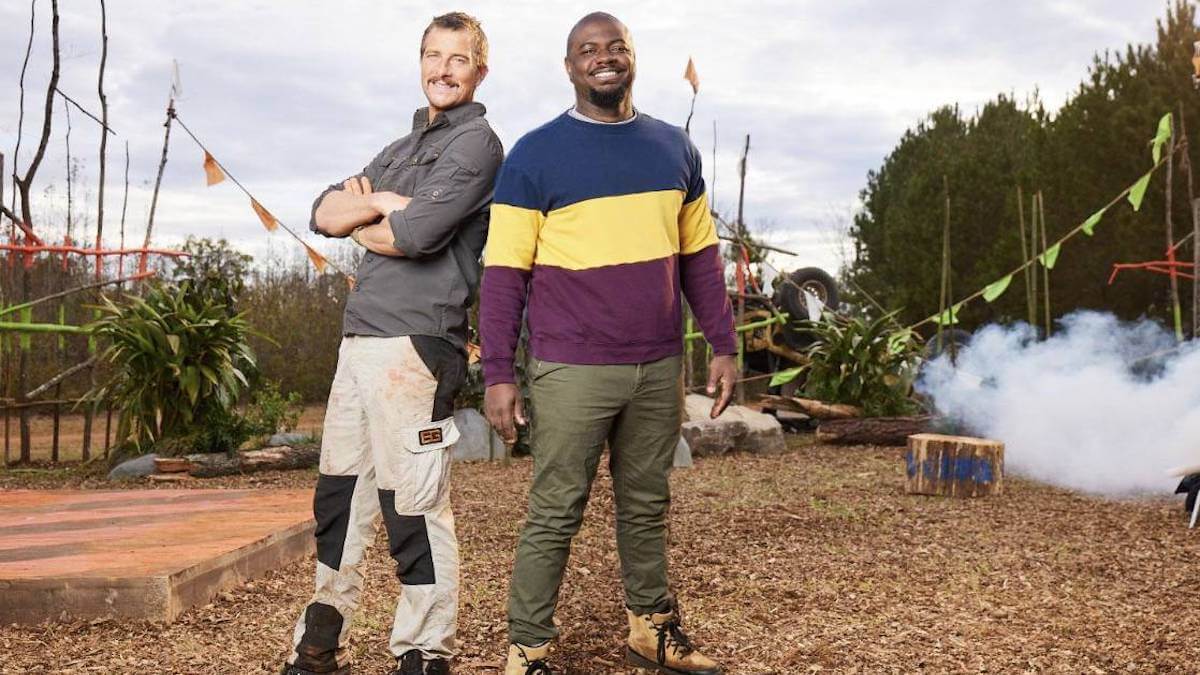 Two men stand back-to-back in a field of obstacle courses.