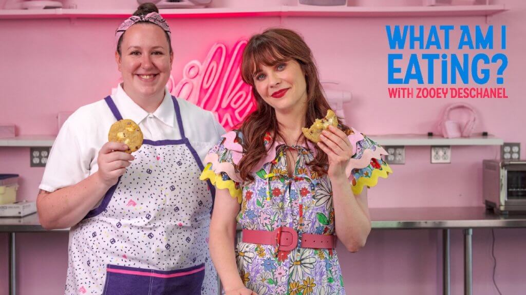 Actor Zooey Deschanel in a pink bakery holding up cookies with a baker