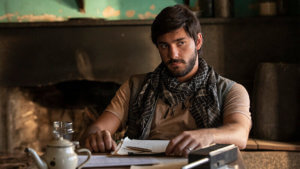 A man reclining by a desk wearing an Arabian style scarf.