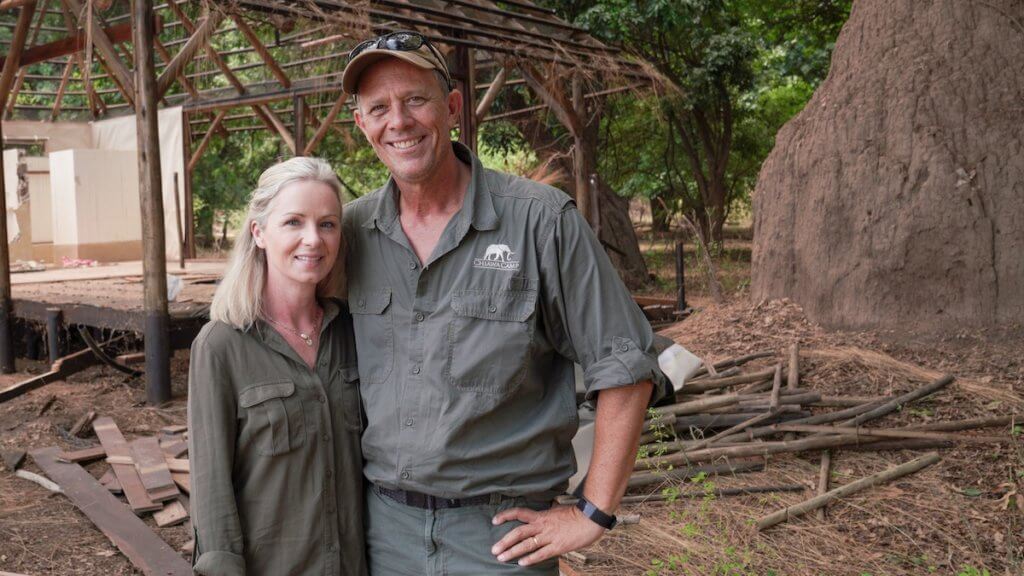 A pair of white safari owners in front of a rundown African structure