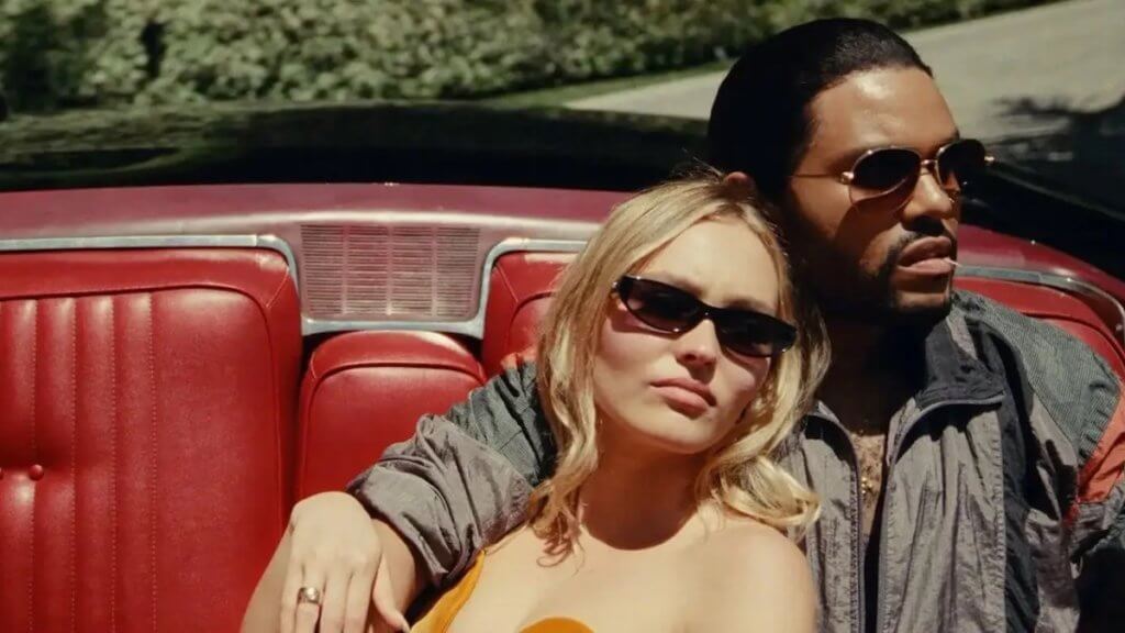 A young woman lounges against a man in a red leather convertible seat