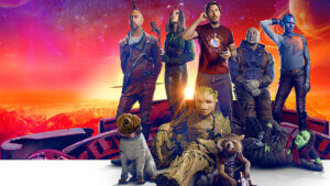 The cast of Guardians of the Galaxy gathered in a casual grouping on top of a ship with a fiery alien sunset behind them.