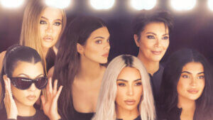 Six women of Kardashian family looking in a vanity mirror with lights over it.